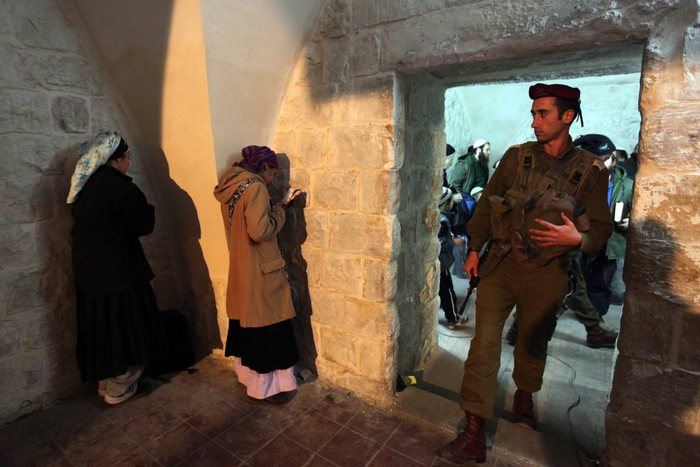 An Israeli soldier enters a room in the Joseph Tomb compound where ultra-Orthodox Jewish women are deep in prayer as hundreds of Jewish settlers and ultra-Orthodox Jewish pilgrims are escorted to Joseph's Tomb, in the West Bank city of Nablus early 28 December 2010. In coordination with the Palestinian forces that control Nabus, the Israeli army escorted hundreds of Jewish settlers to the ancient shrine, believed to be the final resting place of the biblical patriach. The tomb saw fierce fighting a decade ago in the 2nd Intifada and has recently undergone extensive renovations including a new roof. ANSA/KOBI GIDEON ISRAEL OUT
