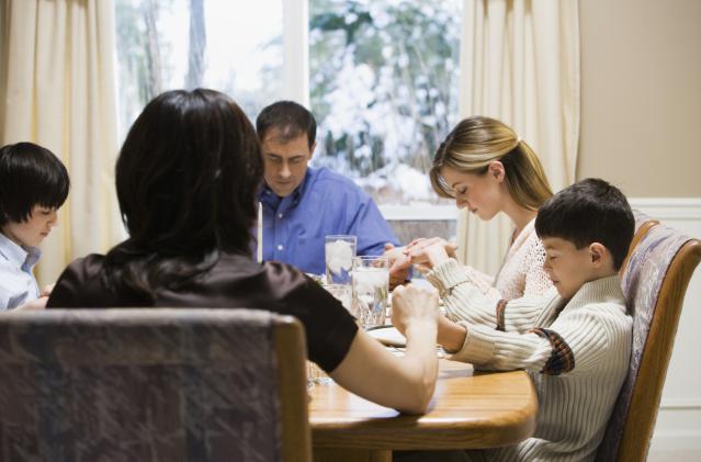 Parents and three children (9-17) praying and holding hands at table